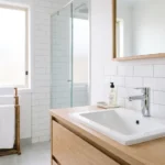 A spotlessly clean modern bathroom with gleaming white tiles, a shiny faucet, fresh towels, and green plants representing bathroom cleaning hacks that work