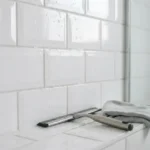 Clean white ceramic bathroom tiles with water droplets and a squeegee, showing tiles free of soap scum