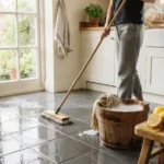 Homemade floor cleaner ingredients including vinegar, baking soda, and lemons beside a mop and bucket on a clean tiled floor