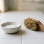 Close up of clean tile floor with baking soda paste and scrub brush used for grout cleaning