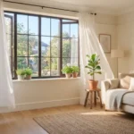 Freshly cleaned white curtains hanging beside a sunlit window in a bright, tidy living room
